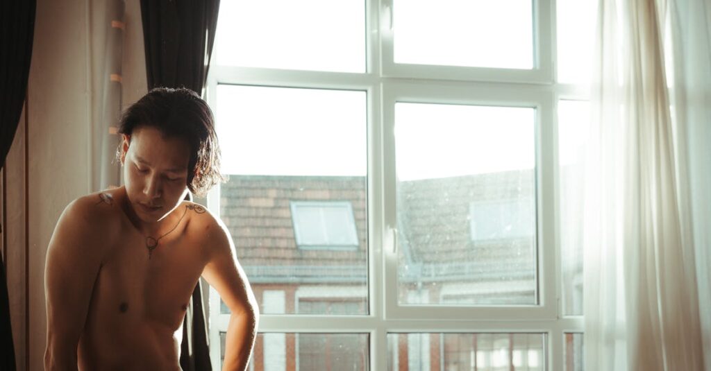 夜明けの光が部屋を満たすなか、窓のそばに立つ男性。こわばっていた肩が、ゆっくりとほどけていく静かな変化。