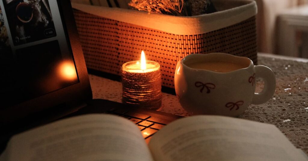 窓辺に置かれた開かれた本とお茶。ろうそくの光があたたかく揺れる、静かな読書の情景。
