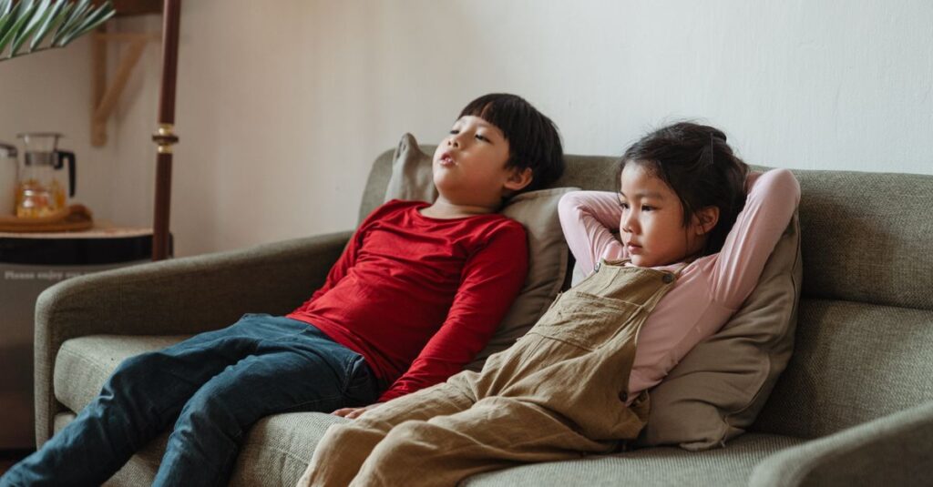 薄暗い部屋で背中合わせに座る双子の子供たち。孤独と警戒が混じる繊細な表情。