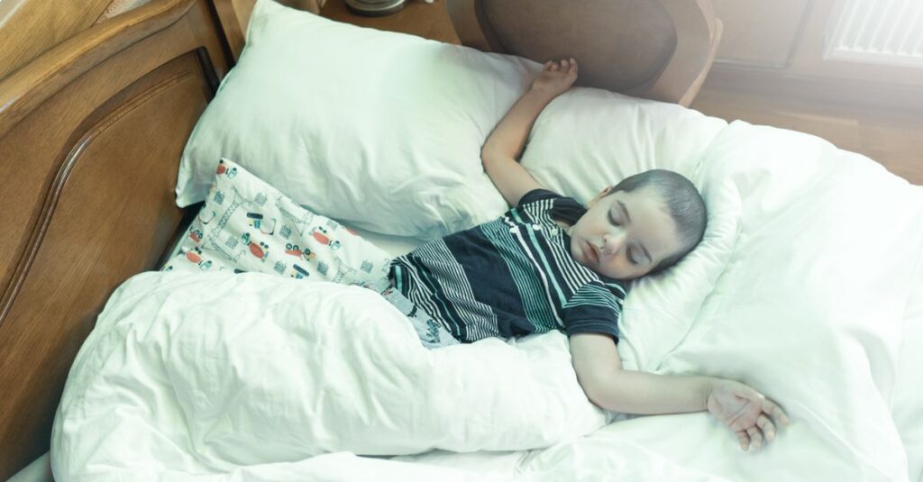 暖炉のそばの椅子で毛布にくるまって眠る子供。誰かがそっとかけてくれたような、安心のぬくもり。