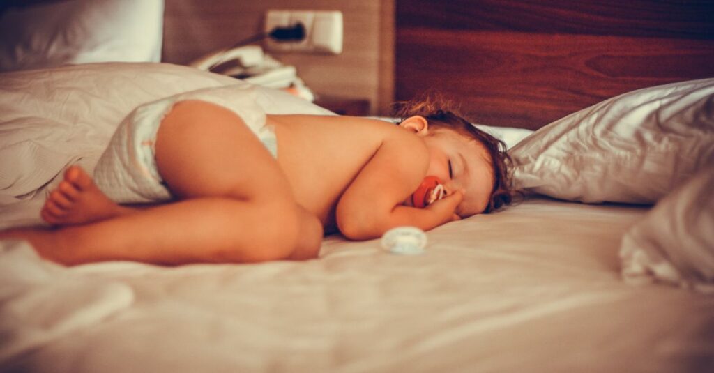 暖炉のそばの椅子で毛布にくるまって眠る子供。誰かがそっとかけてくれたような、安心のぬくもり。