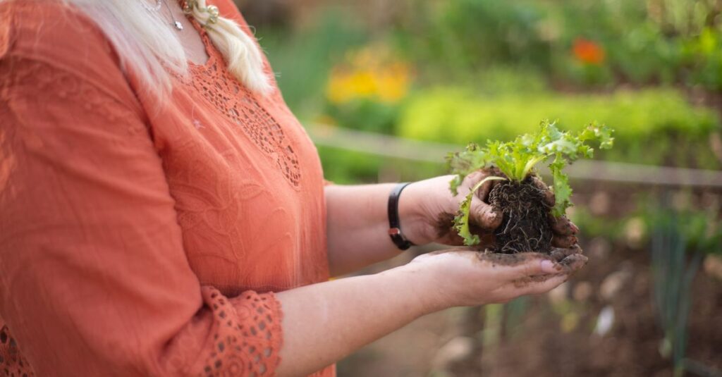 庭にひざをつき、両手で丁寧に苗を植える女性。その表情には決意と希望が宿っている。