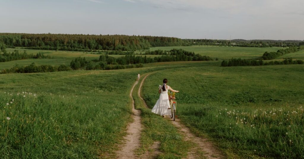 小道の脇でゆっくり花を摘む女性。急がない旅の穏やかな豊かさを象徴する風景。
