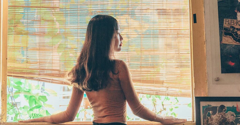 感情を抑えながら静かに過ごす女性。我慢が当たり前になった日々を象徴する風景。
