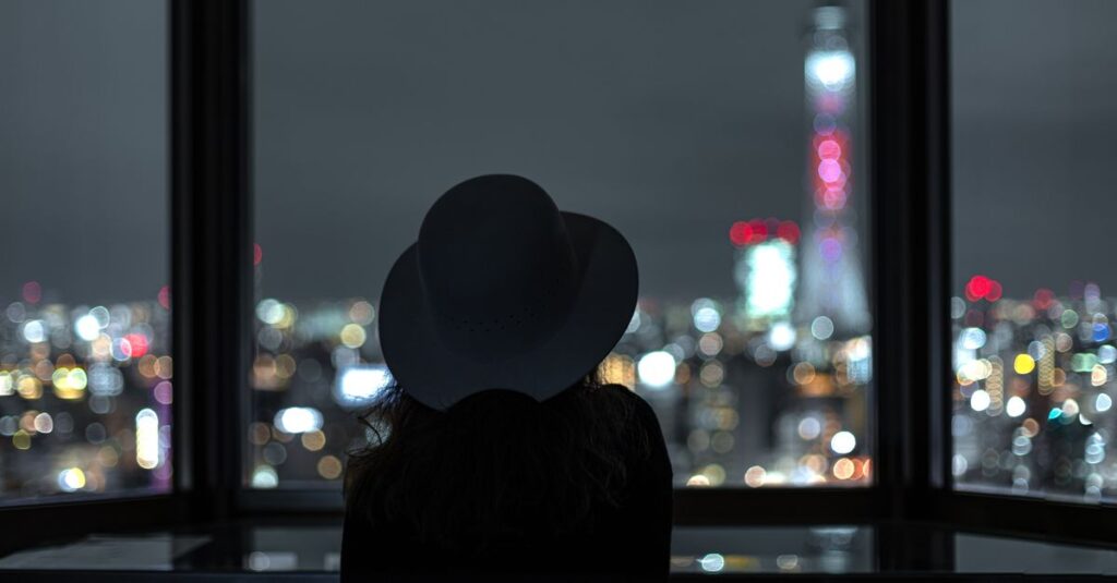 夜の街の光をひとり見つめる女性。未来の不安と静かに向き合いながら、自分の心の声を探している。