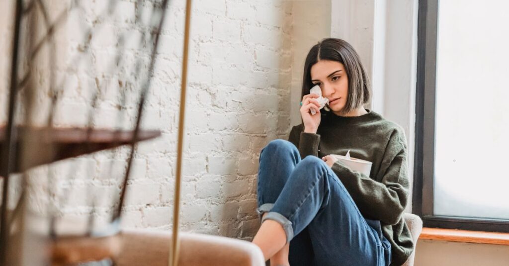 感情を抑えながら静かに過ごす女性。我慢が当たり前になった日々を象徴する風景。