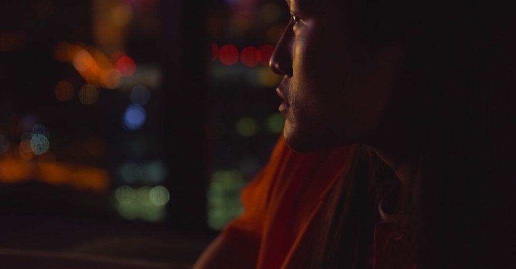 夜の街の光をひとり見つめる女性。未来の不安と静かに向き合いながら、自分の心の声を探している。