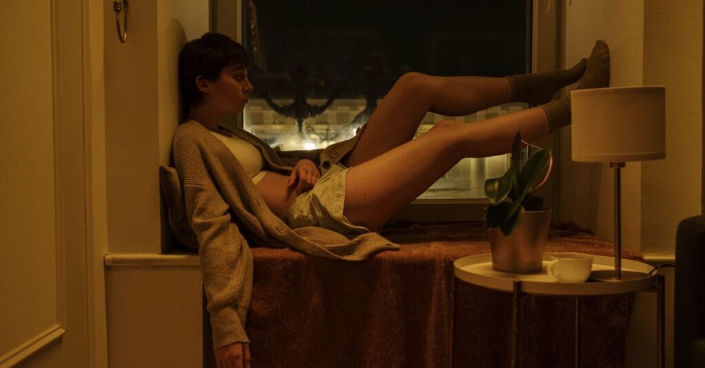 他者の重さまで背負いながら静かに立つ女性。境界線があいまいになった優しさの消耗を象徴する風景。